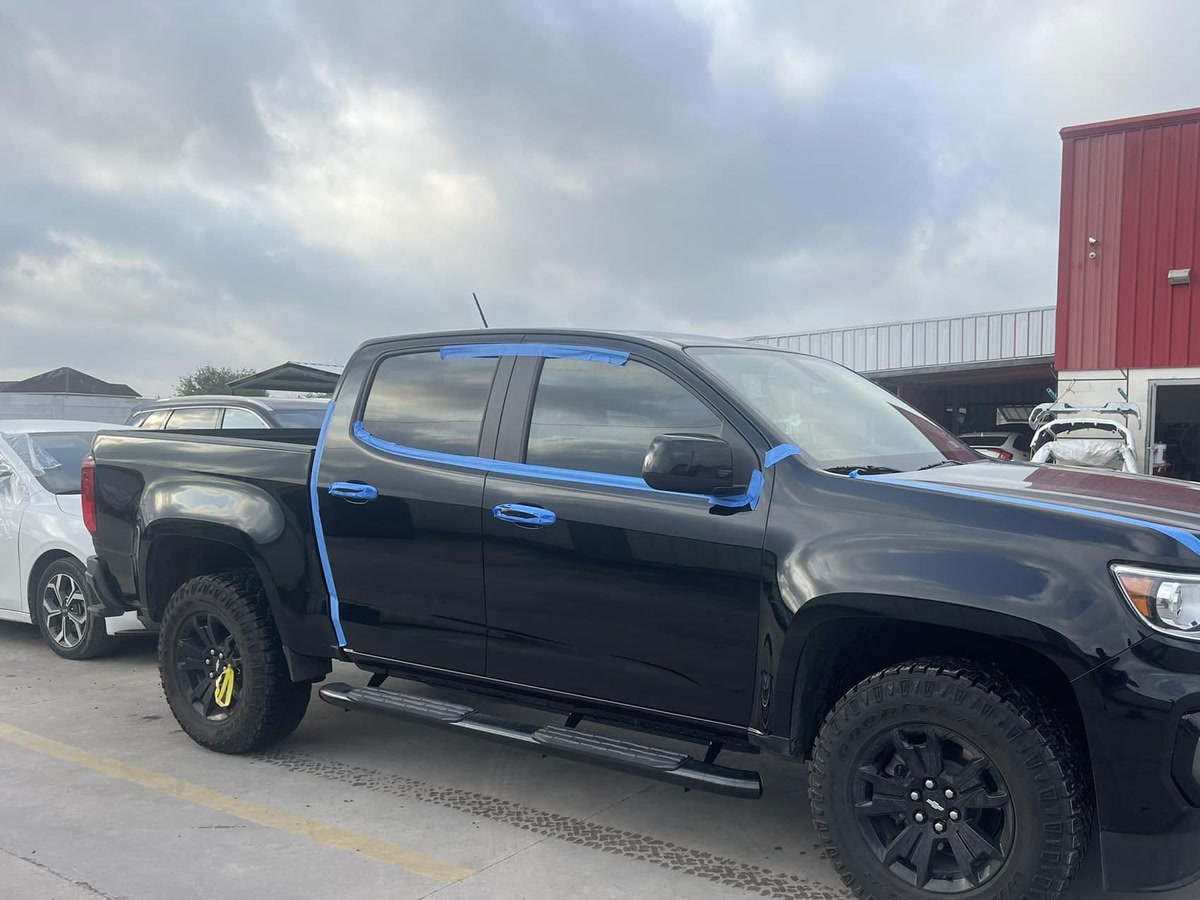 A pickup with its window frames taped off, parked outside the shop bay at Superior Collision in Brownsville, TX
