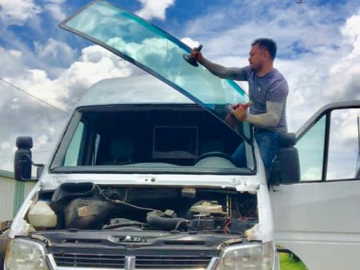 A technician lowering a replacement windshield into place on a van at Superior Collision in Brownsville, TX